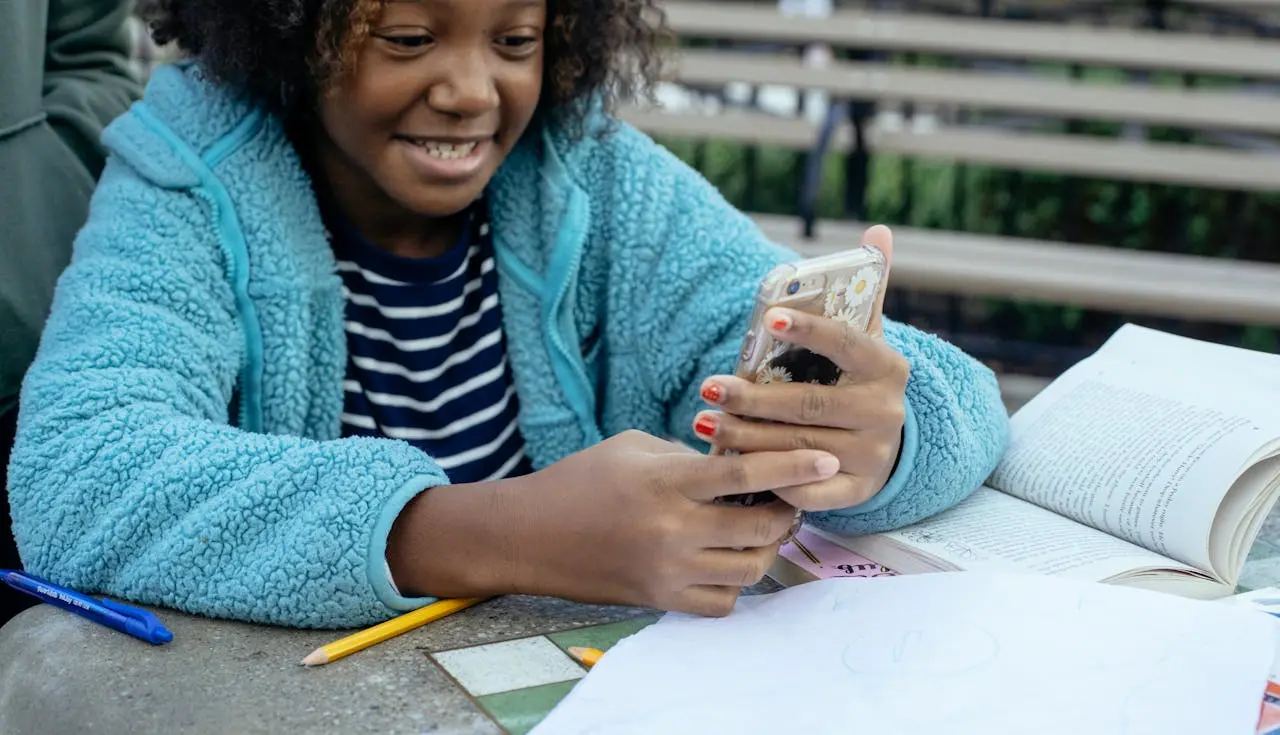 Criança preta, fazendo lição de casa e aprendendo com gamificação em jogos pedagógicos através do celular.