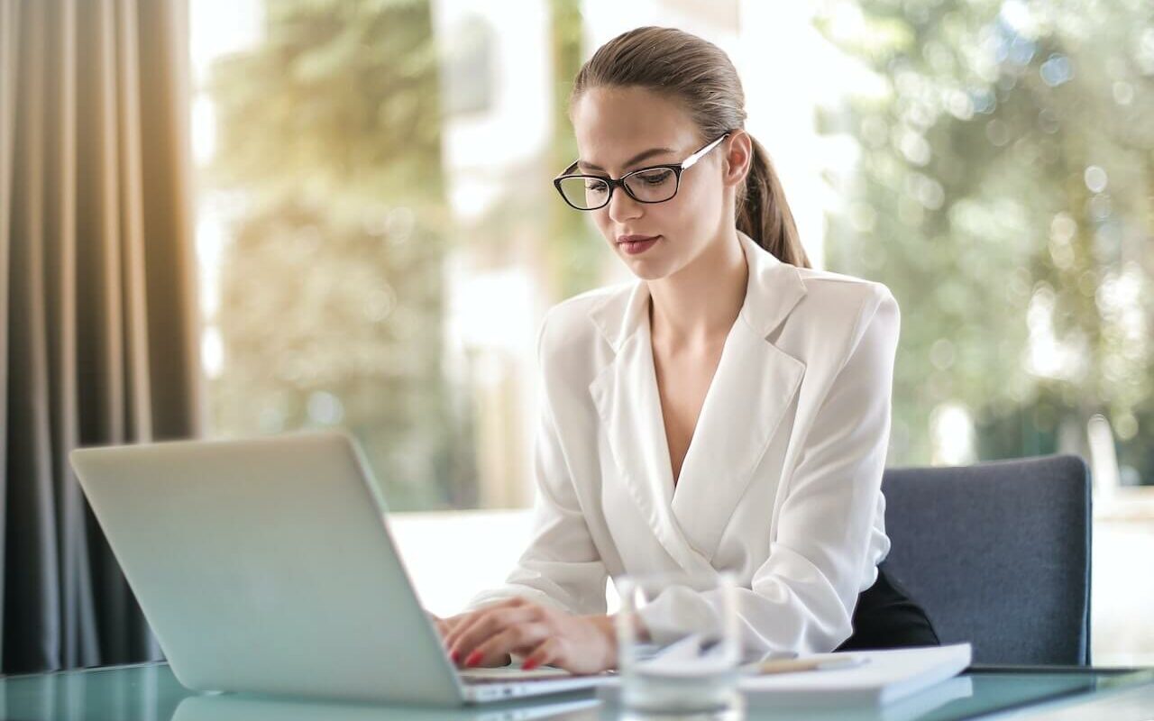 Mulher em ambiente profissional trabalhando sentada em mesa de escritório seguindo os exemplos de postura profissional.