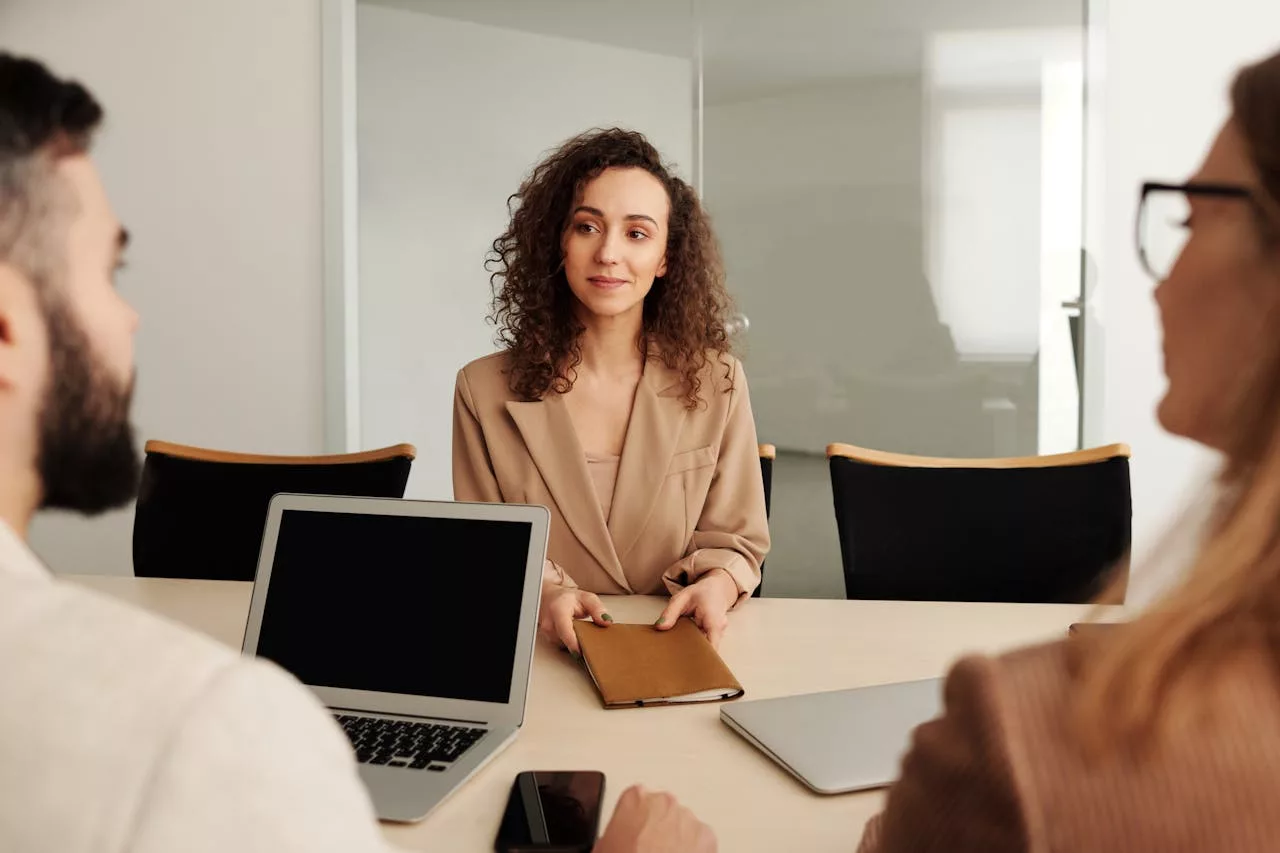 Mulher de cabelos cacheados fazendo uma entrevista com o Talent-acquisition, Dois funcionarios na lateral trazendo os profissionais certos para a sua equipe, atraindo e retendo funcionários qualificados e alinhados ao perfil da sua empresa